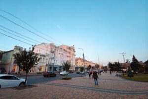 Ulica miasta z zabytkowymi budynkami, piesi i samochody.