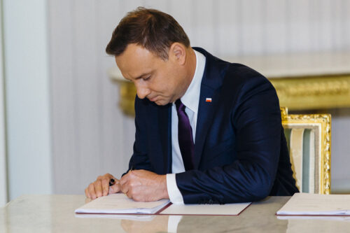 Mężczyzna w garniturze podpisuje dokument na biurku.