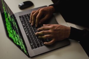 Osoba programująca na laptopie z zielonym kodem