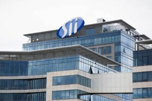 Nowoczesny szklany biurowiec z logo firmy na dachu.