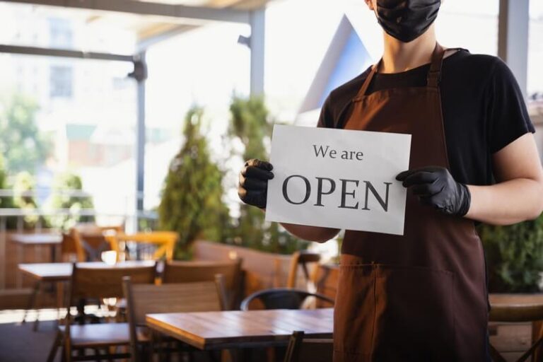 Pracownik restauracji z tabliczką 'Otwarta' na tarasie.