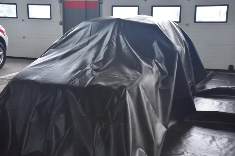 Samochód przykryty plandeką w garażu.