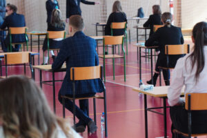 Uczniowie piszący egzamin w sali gimnastycznej.