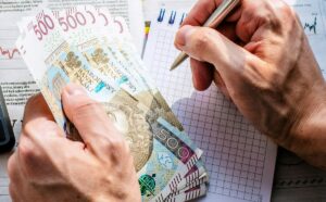 Osoba liczy polskie banknoty przy notatniku.