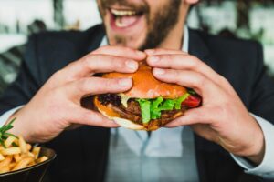 Człowiek jedzący burgera z frytkami na talerzu.
