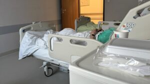 Pacjent leży w szpitalnym łóżku na sali.