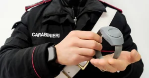 Policjant trzyma elektroniczną bransoletę nadzorującą.