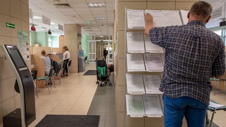 Wnętrze biura z dokumentami i osobami siedzącymi.