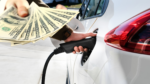 Ładowanie samochodu elektrycznego i dolary w ręku.