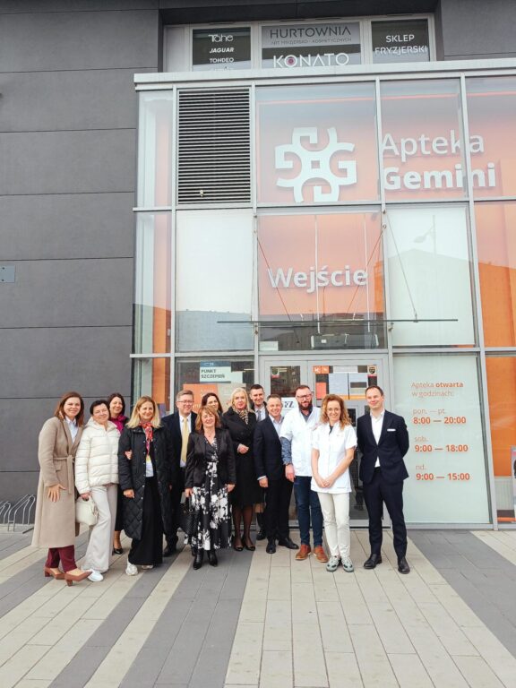 Grupa osób przed Apteką Gemini w Polsce.