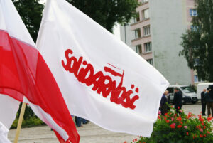 Flaga Solidarności obok polskiej flagi na tle budynków.