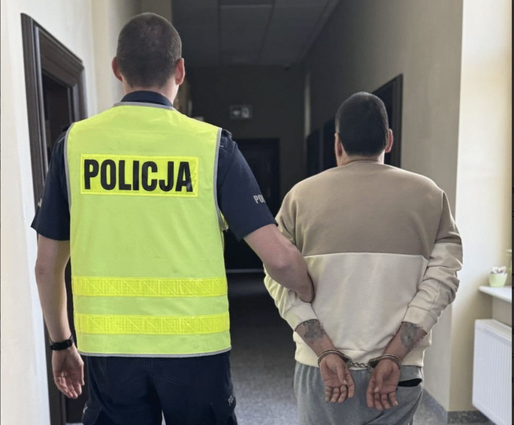 Policjant prowadzi zatrzymanego w kajdankach.