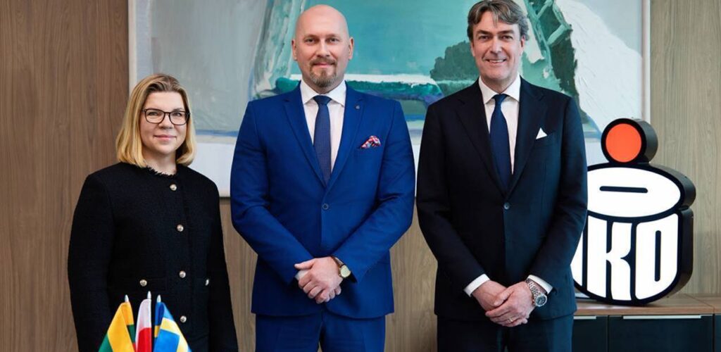 Trzy osoby stoją przy stole z flagami.