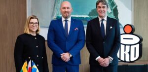 Trzy osoby stoją przy stole z flagami.