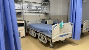 Łóżko szpitalne z niebieską pościelą i sprzętem medycznym.