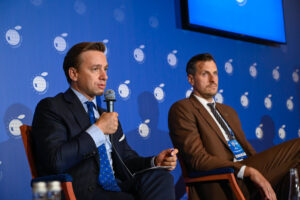 Dwaj mężczyźni podczas panelu konferencyjnego na niebieskiej scenie
