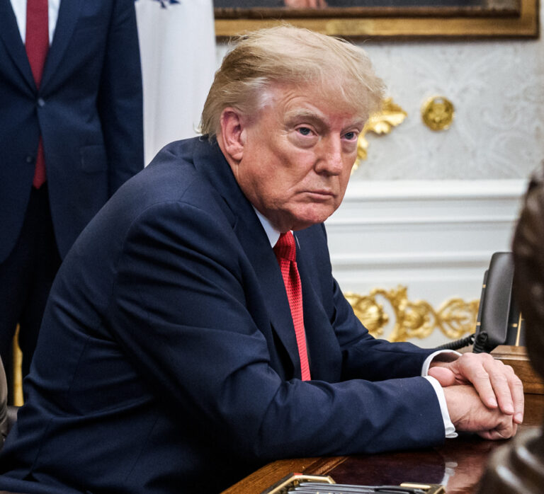 Donald Trump siedzi przy biurku w garniturze.