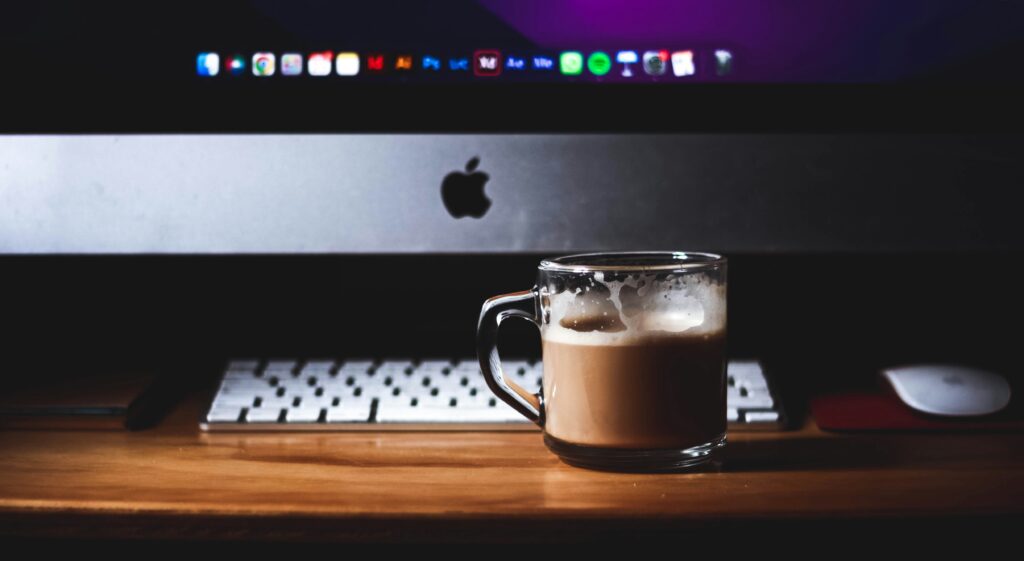 Kubek kawy przed laptopem Apple na drewnianym biurku