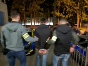 Policjanci prowadzą zatrzymanego mężczyznę nocą do radiowozu.