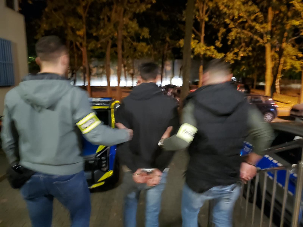 Policjanci prowadzą zatrzymanego mężczyznę nocą do radiowozu.