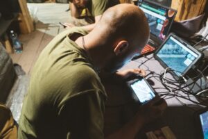 Mężczyzna obsługuje smartfon przy stole z laptopami