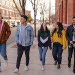 Grupa młodych ludzi spaceruje po miejskim chodniku.