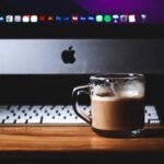 Kubek kawy przed laptopem Apple na drewnianym biurku