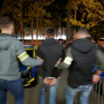Policjanci prowadzą zatrzymanego mężczyznę nocą do radiowozu.