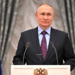 Mężczyzna przy mównicy z rosyjską flagą